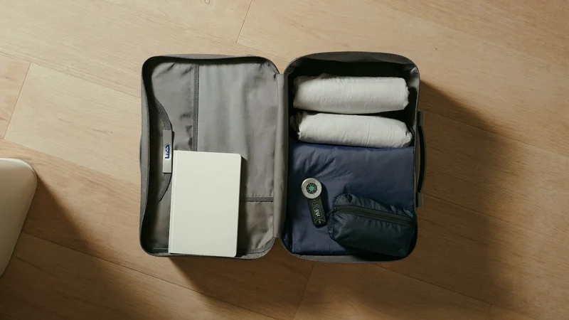 Illustrierte Draufsicht auf eine Reisetasche mit gerollter Kleidung, Kompass und kleiner Notfalltasche